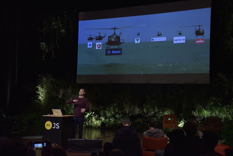 Adrian Holovaty in front of the giant screen showing a picture of heavy helicopters with a logo of many frameworks on top of them