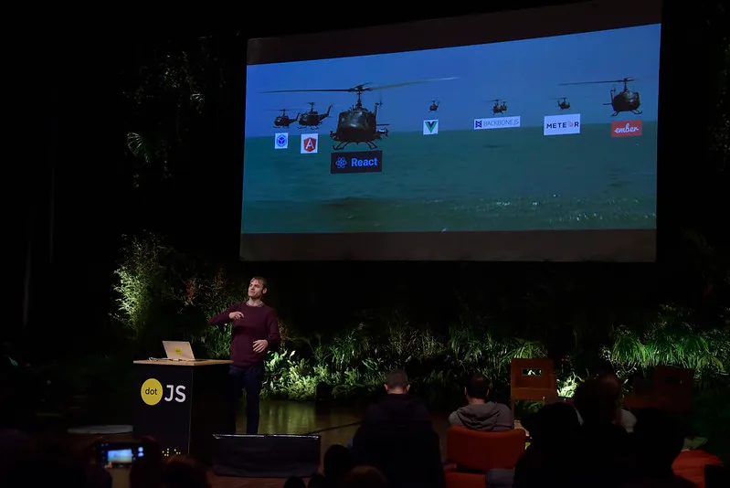 Adrian Holovaty in front of the giant screen showing a picture of heavy helicopters with a logo of many frameworks on top of them