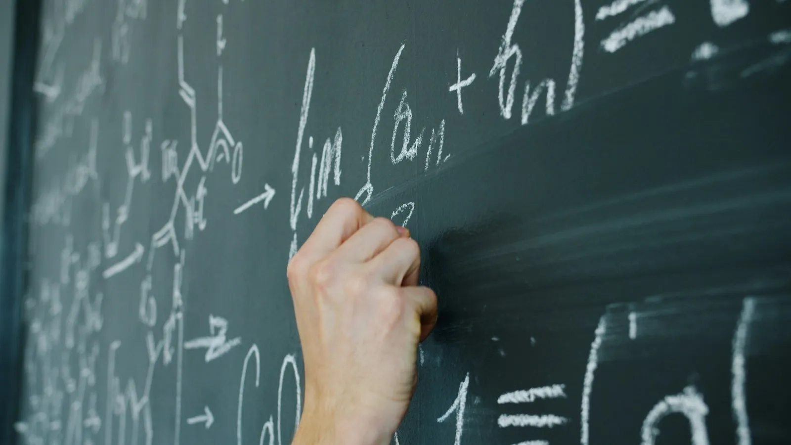 A hand writing equations on a chalkboard