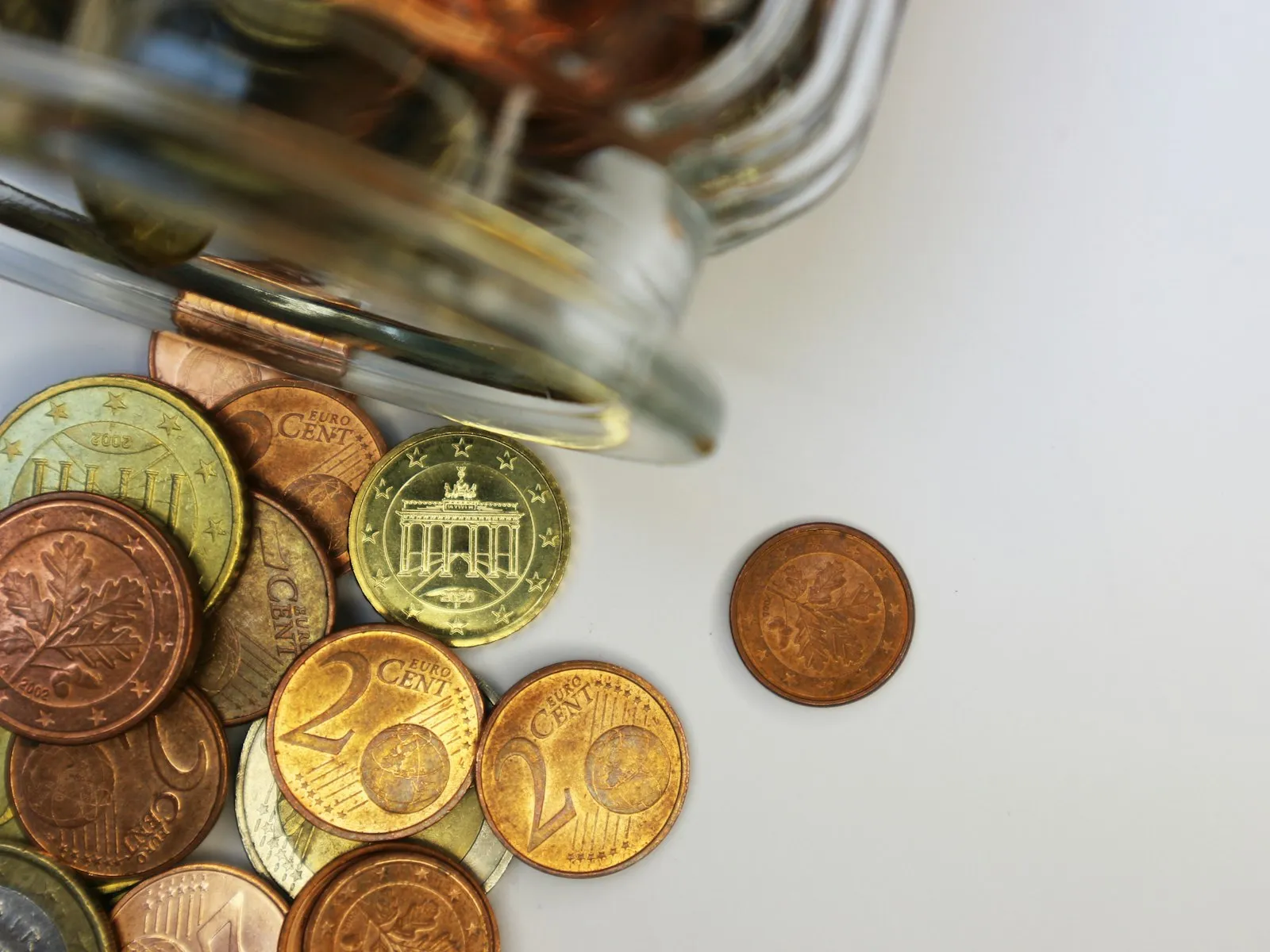 Euro coins spilling from a jar, with one cent set apart